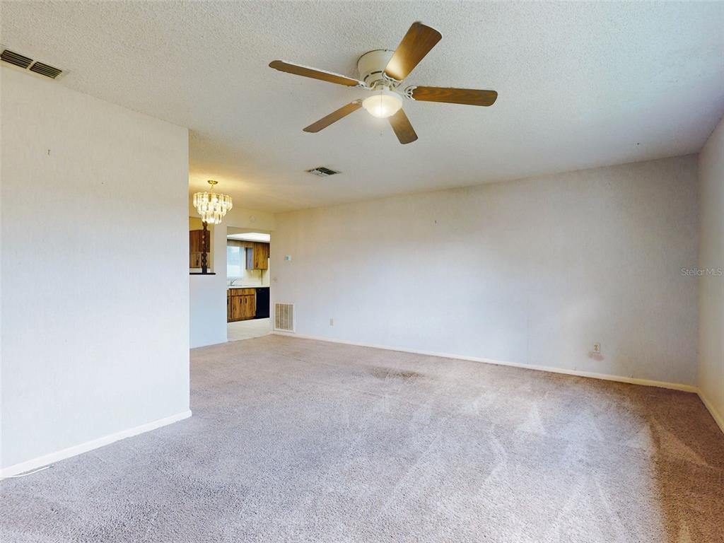 A carpeted living room with a ceiling fan leads to a kitchen with wood cabinets — 1362 WOODBINE AVENUE, DELTONA, FL