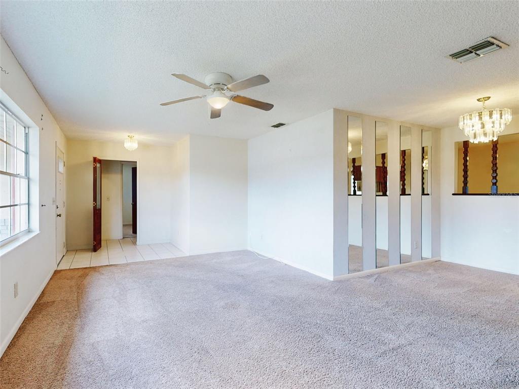 A carpeted living room features a ceiling fan, mirrored wall panels, and a crystal chandelier — 1362 WOODBINE AVENUE, DELTONA, FL