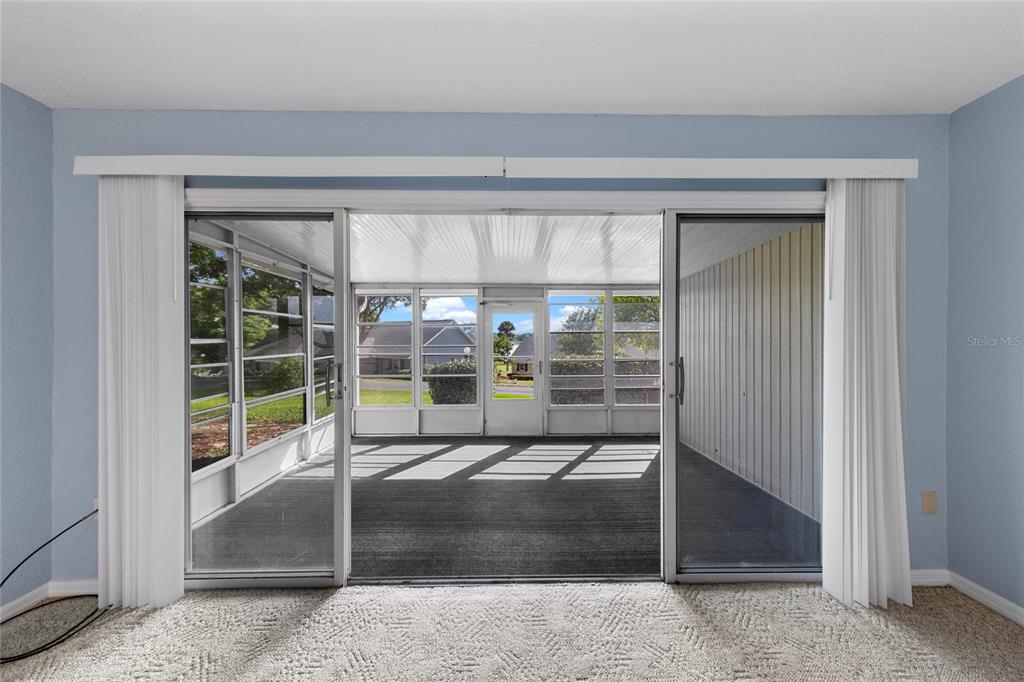A carpeted room looks through sliding glass doors onto a screened-in porch with outdoor views — 1337 VILLA LANE UNIT 49, APOPKA, FL