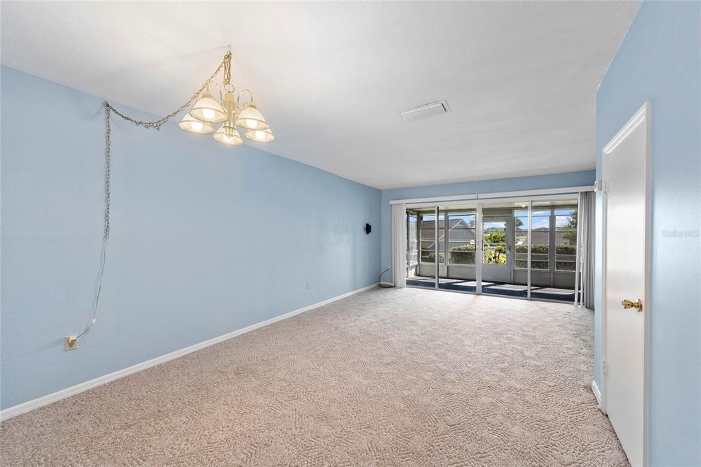 A living room with light blue walls, beige carpet, a chandelier, and sliding glass doors — 1337 VILLA LANE UNIT 49, APOPKA, FL