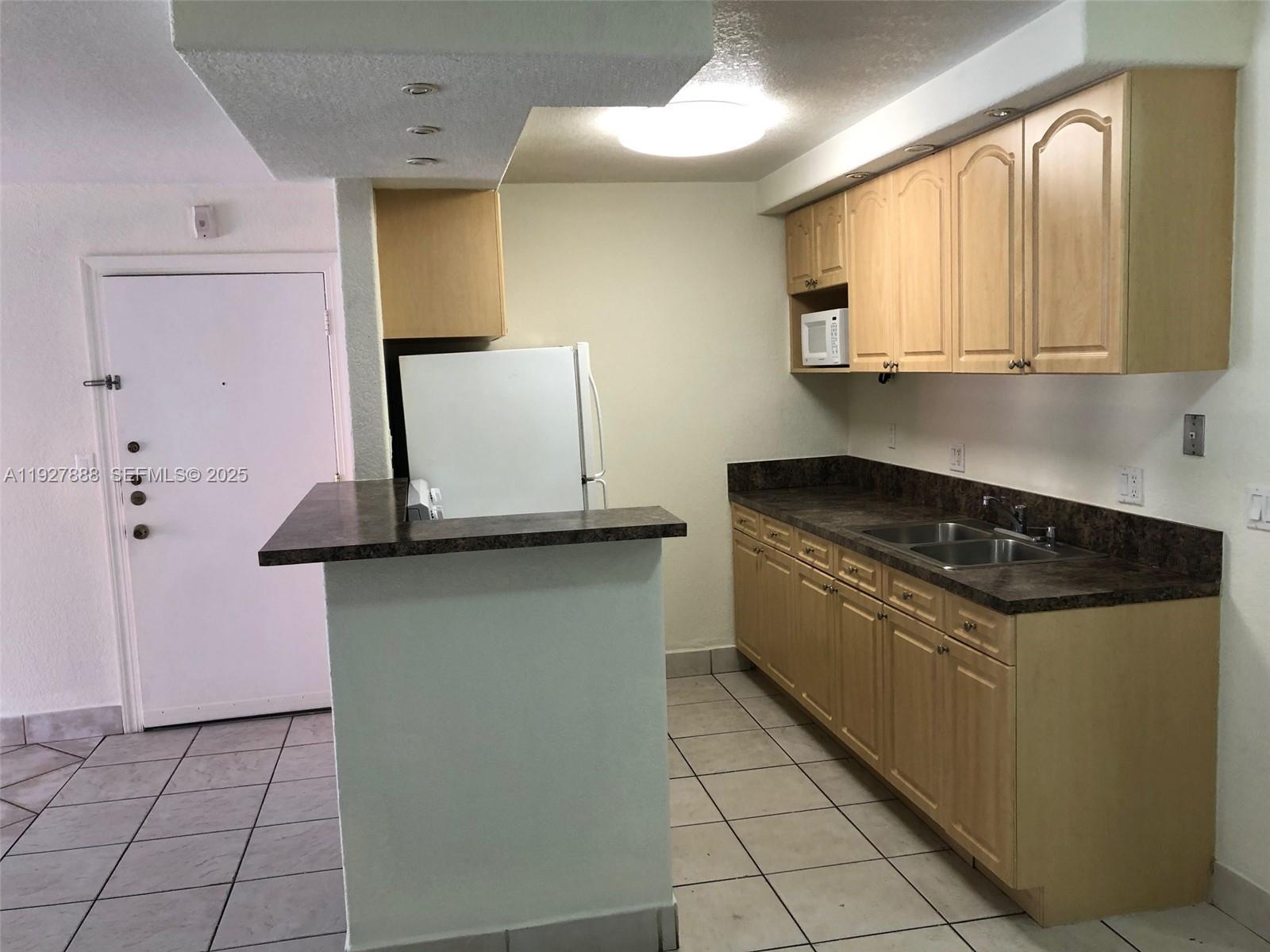 A kitchen features light wood cabinets, dark countertops, a white refrigerator, and tiled flooring — 10744 N Kendall Dr # 16, Miami FL 33176, MIAMI, FL
