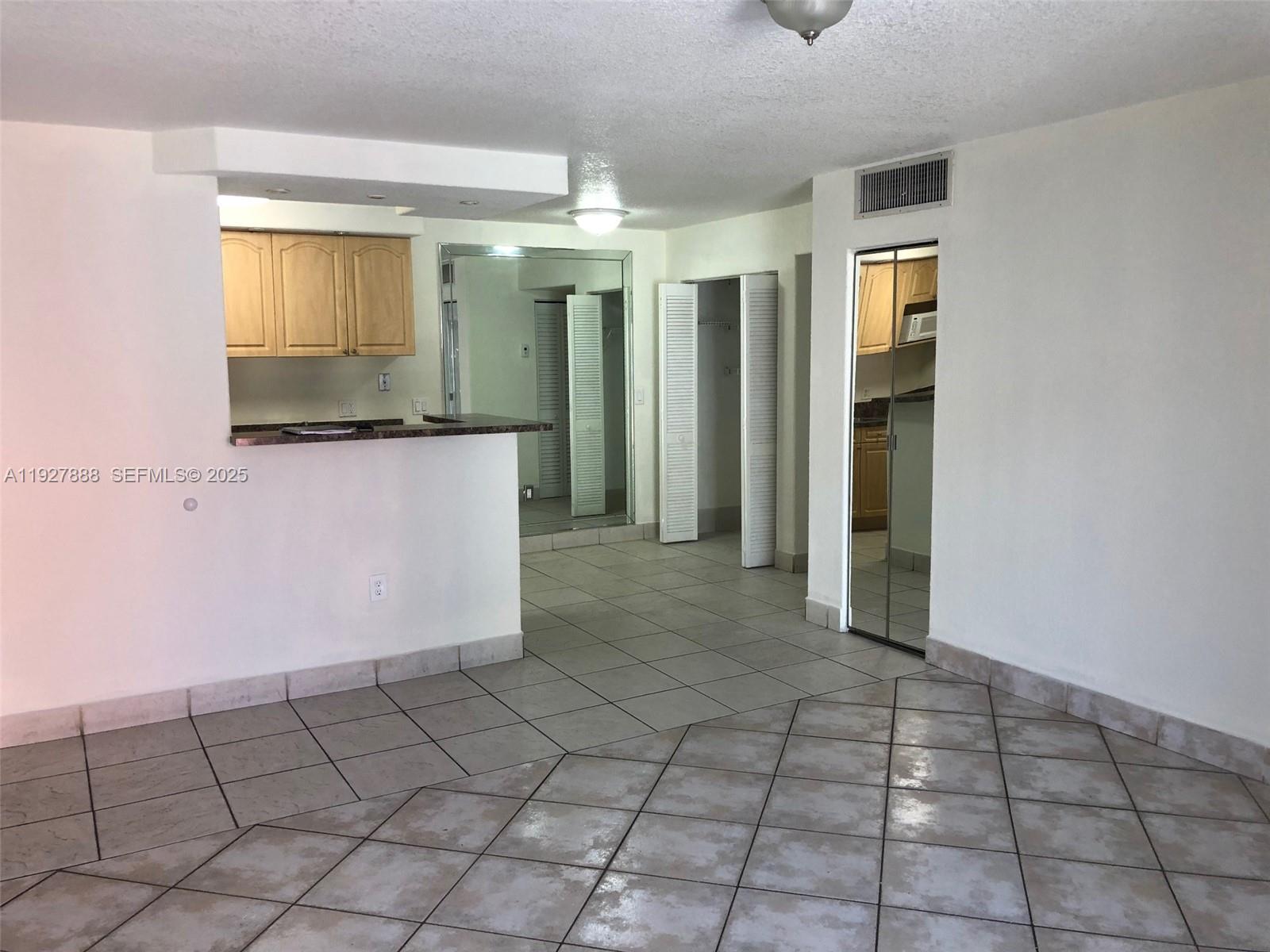 An interior view shows a tiled room with a kitchen pass-through and mirrored closet doors — 10744 N Kendall Dr # 16, Miami FL 33176, MIAMI, FL