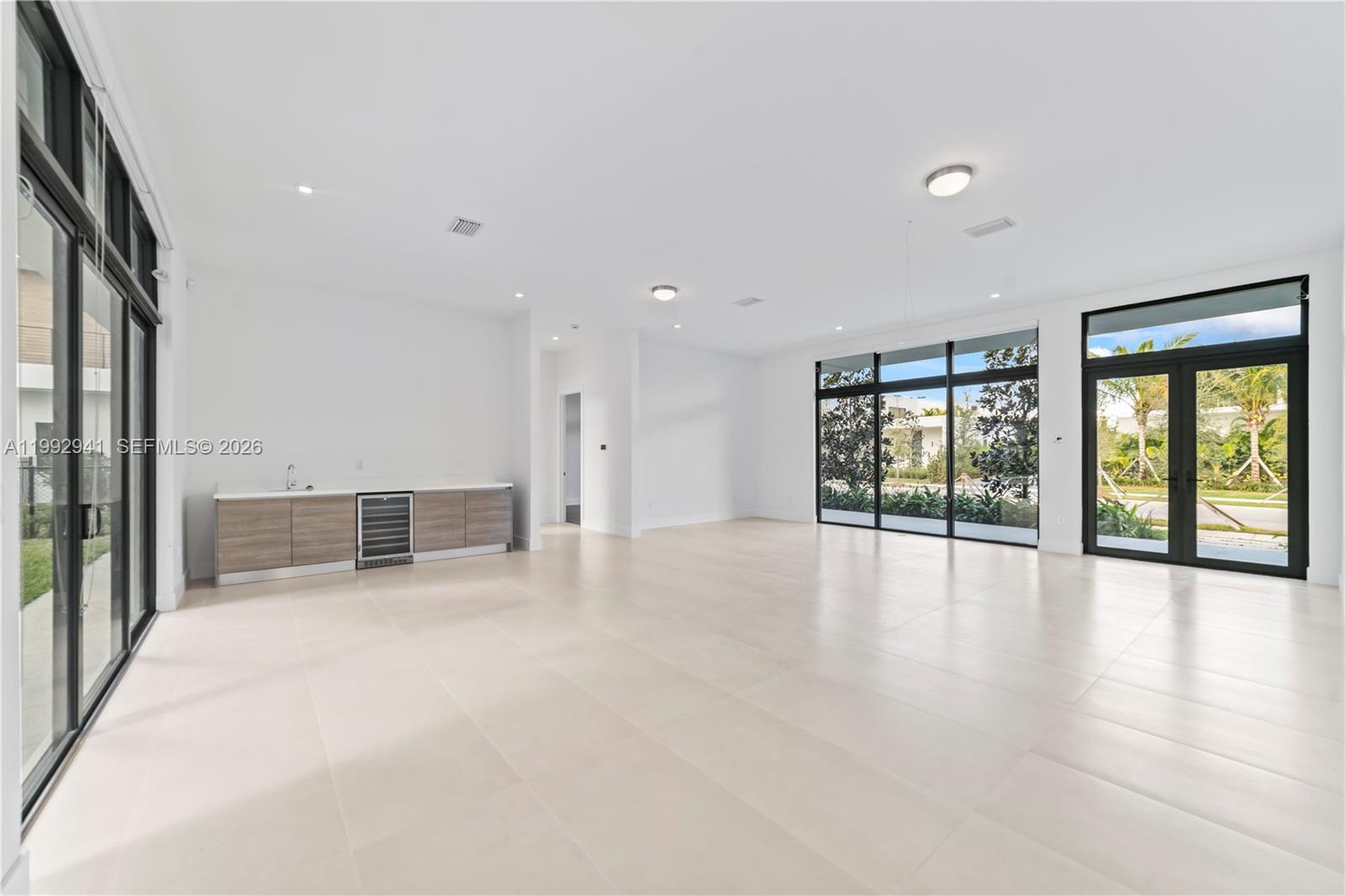 A bright, minimalist room features light tile floors, a wet bar, and large glass doors — 16680 N Botaniko Dr N # 16680, Weston FL 33326, WESTON, FL
