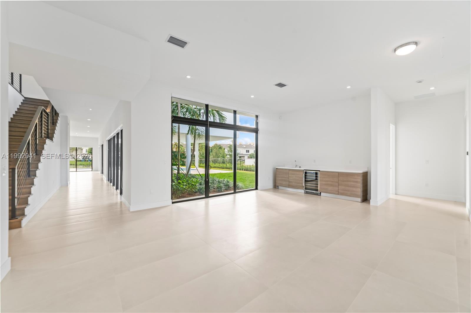 A modern, minimalist living area features large glass doors, light tile floors, and a wet bar — 16680 N Botaniko Dr N # 16680, Weston FL 33326, WESTON, FL