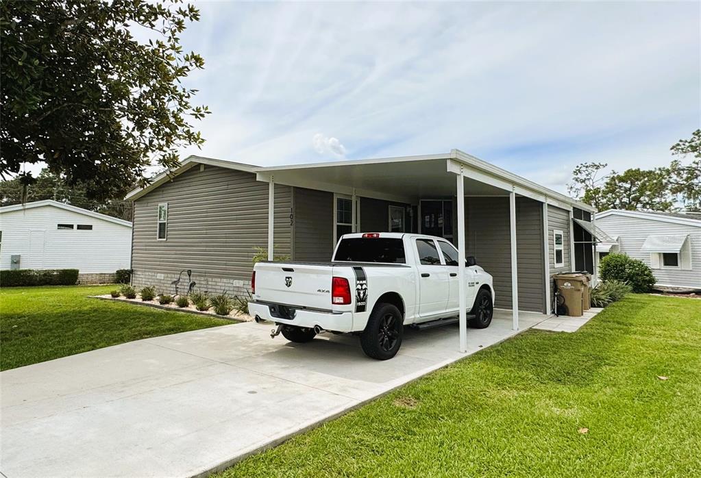 A white pickup truck is parked under a carport attached to a gray mobile home — 102 DOGWOOD TRAIL, LEESBURG, FL