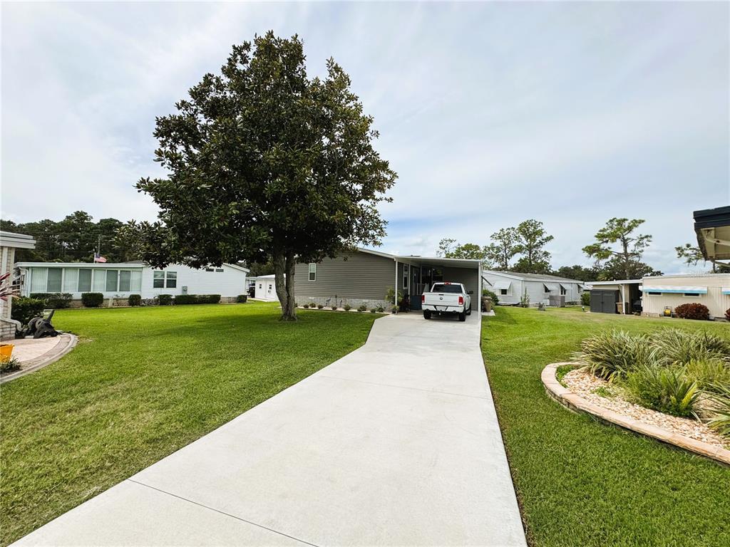 A single-story mobile home with a concrete driveway, a large tree, and a carport — 102 DOGWOOD TRAIL, LEESBURG, FL