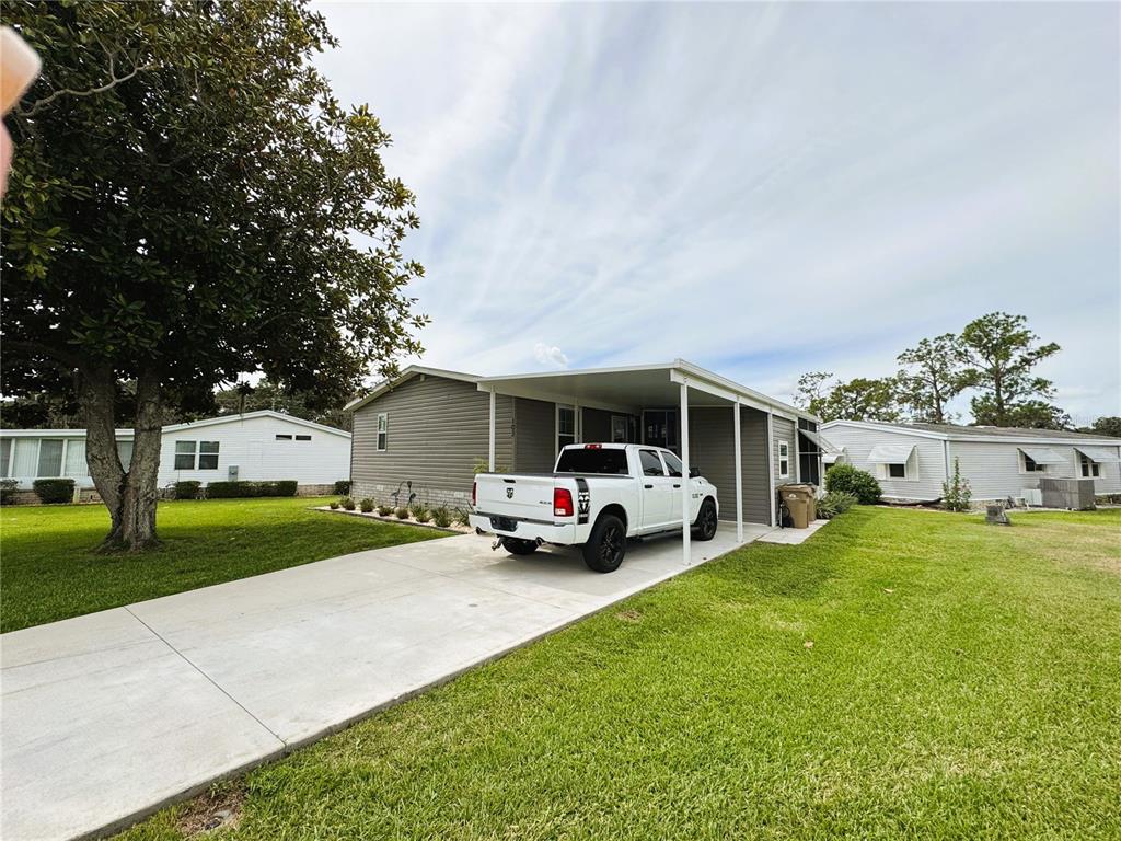 A white pickup truck is parked under a carport attached to a gray mobile home — 102 DOGWOOD TRAIL, LEESBURG, FL