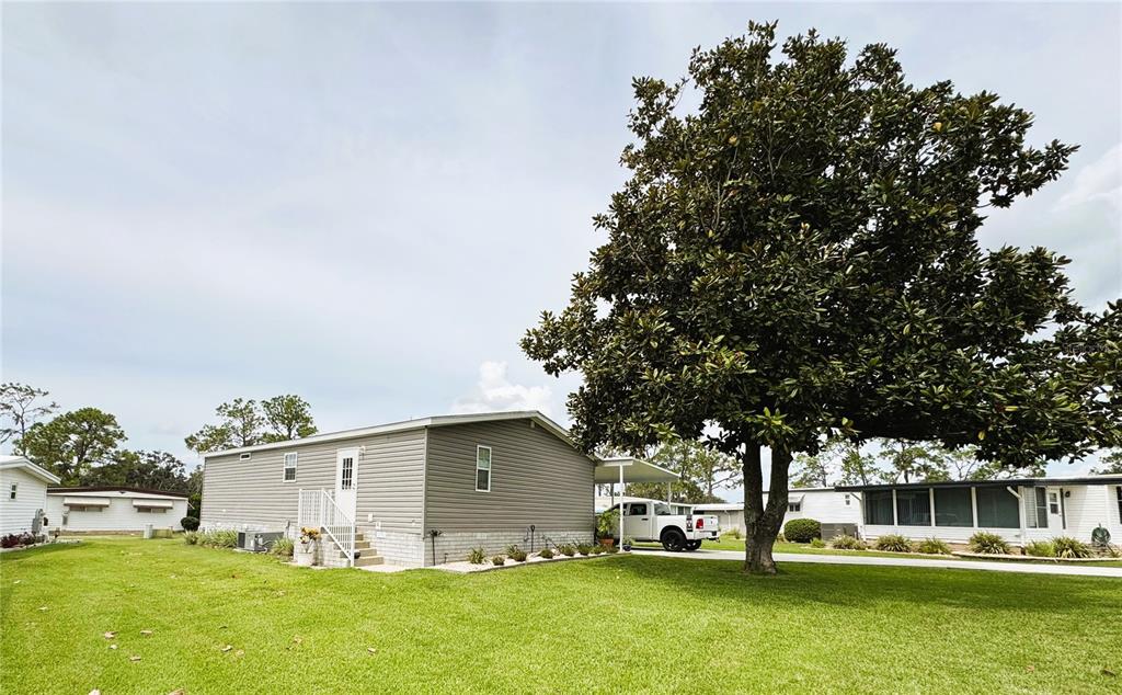 A gray manufactured home sits on a grassy lot next to a large, mature tree — 102 DOGWOOD TRAIL, LEESBURG, FL