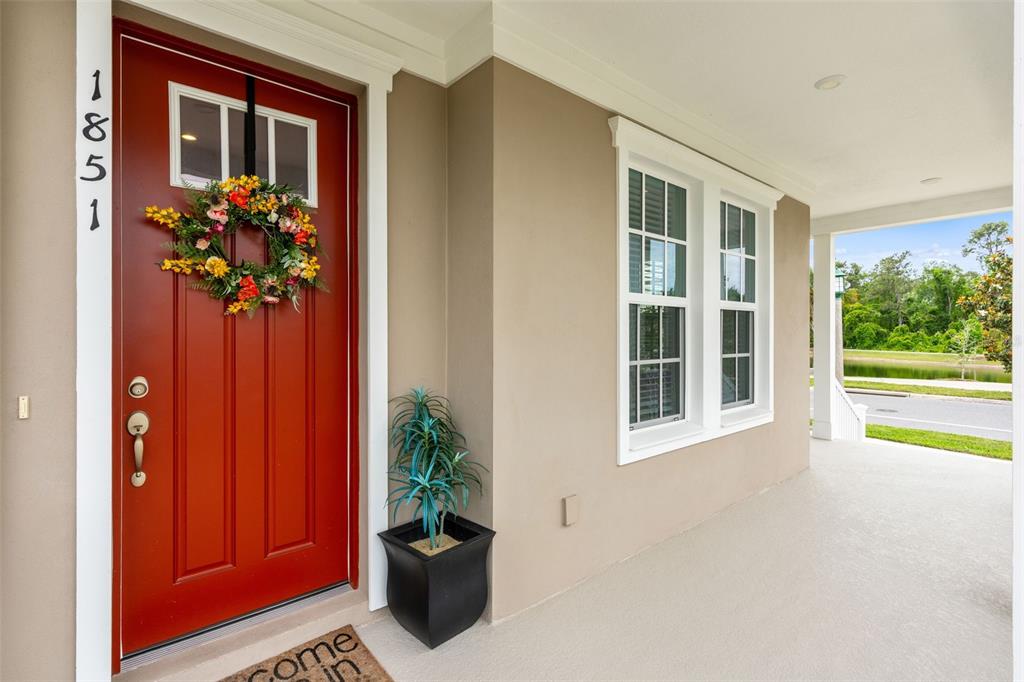 A two-story beige house with a wrap-around front porch and a red front door — 1851 COASTAL COURT, CELEBRATION, FL
