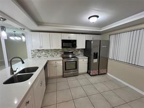 A kitchen with white cabinets, stainless steel appliances, a tile backsplash, and a double sink — 8040 Hampton Boulevard # 104, North Lauderdale FL 33068, NORTH LAUDERDALE, FL