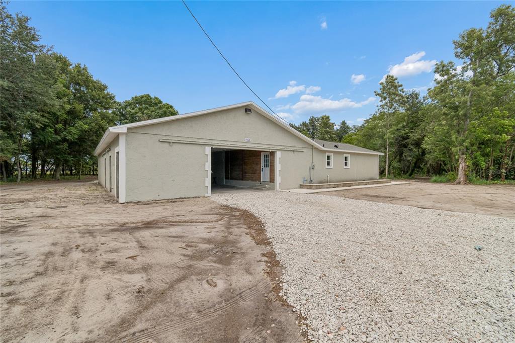 A light-colored, single-story building with a gravel driveway and an open-air garage bay — 15628 CARLTON LAKE ROAD, WIMAUMA, FL