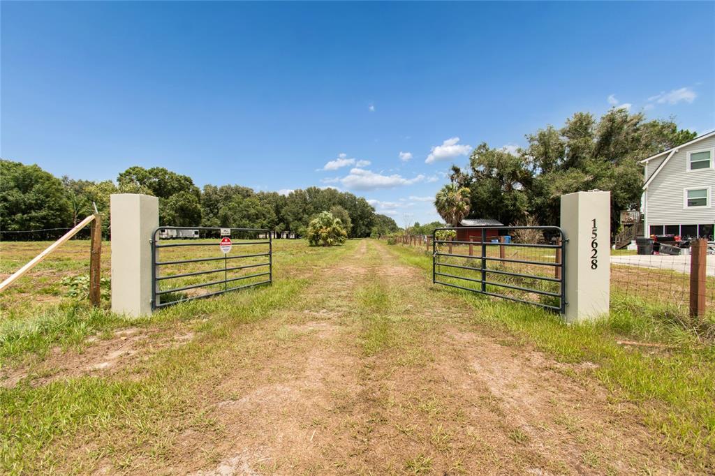 A dirt driveway leads through an open metal gate between two concrete pillars — 15628 CARLTON LAKE ROAD, WIMAUMA, FL