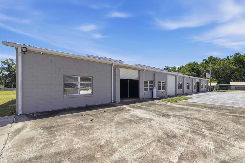 A gray concrete block commercial building with multiple roll-up doors and windows under a blue sky — 943 NW 17TH AVENUE, OCALA, FL