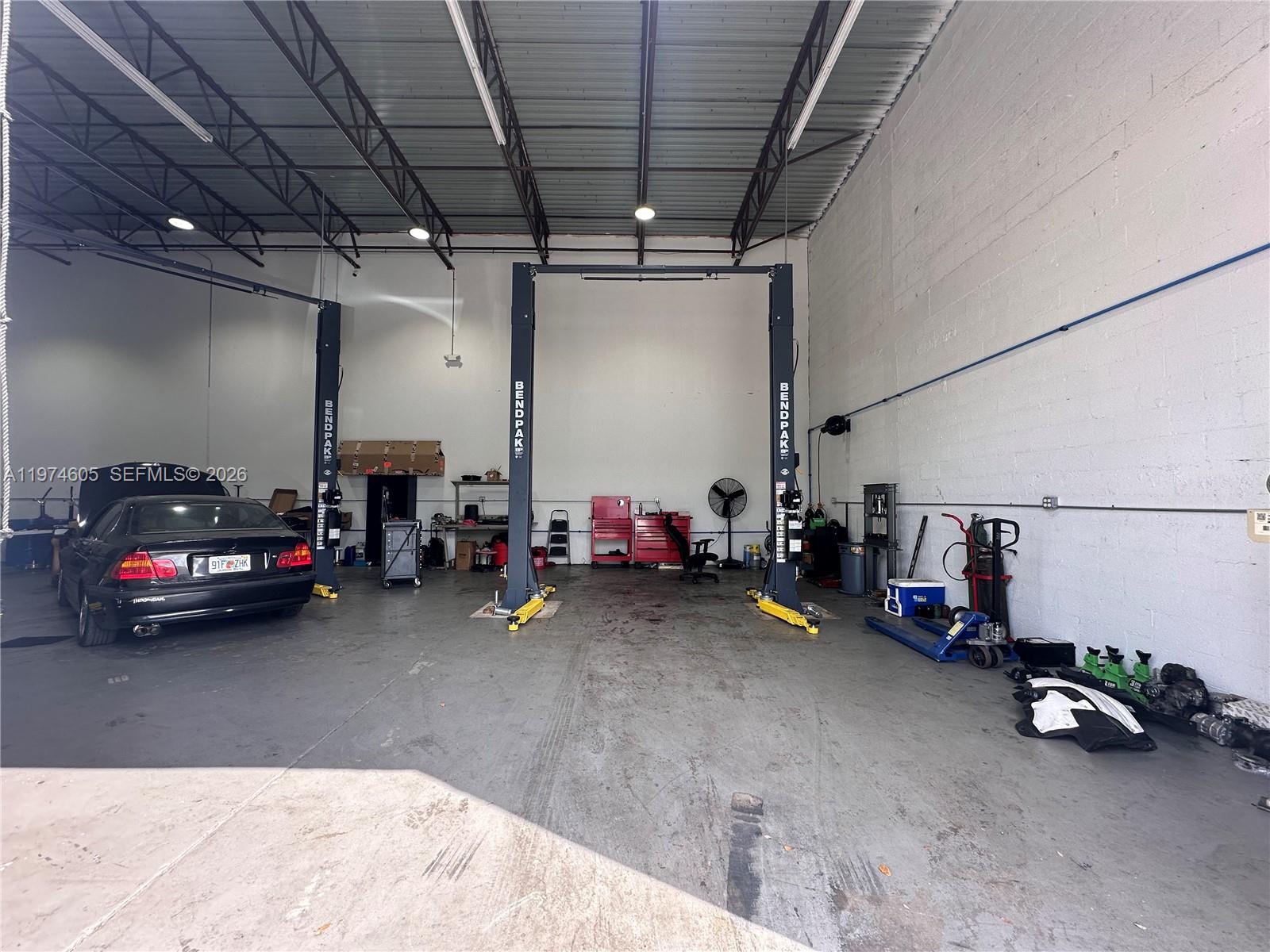 An auto repair shop interior features two BendPak vehicle lifts and a parked black sedan — 3136 John P Curci Dr, Hallandale Beach FL 33009, HALLANDALE BEACH, FL