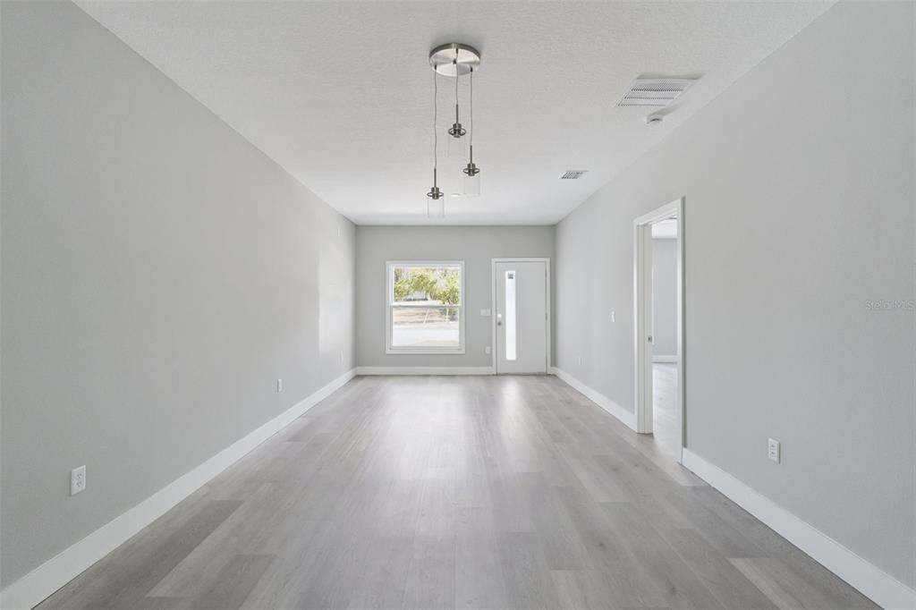 A long, empty room with light gray walls, wood-look flooring, and a modern pendant light — 397 NORTH BOULEVARD W, DAVENPORT, FL