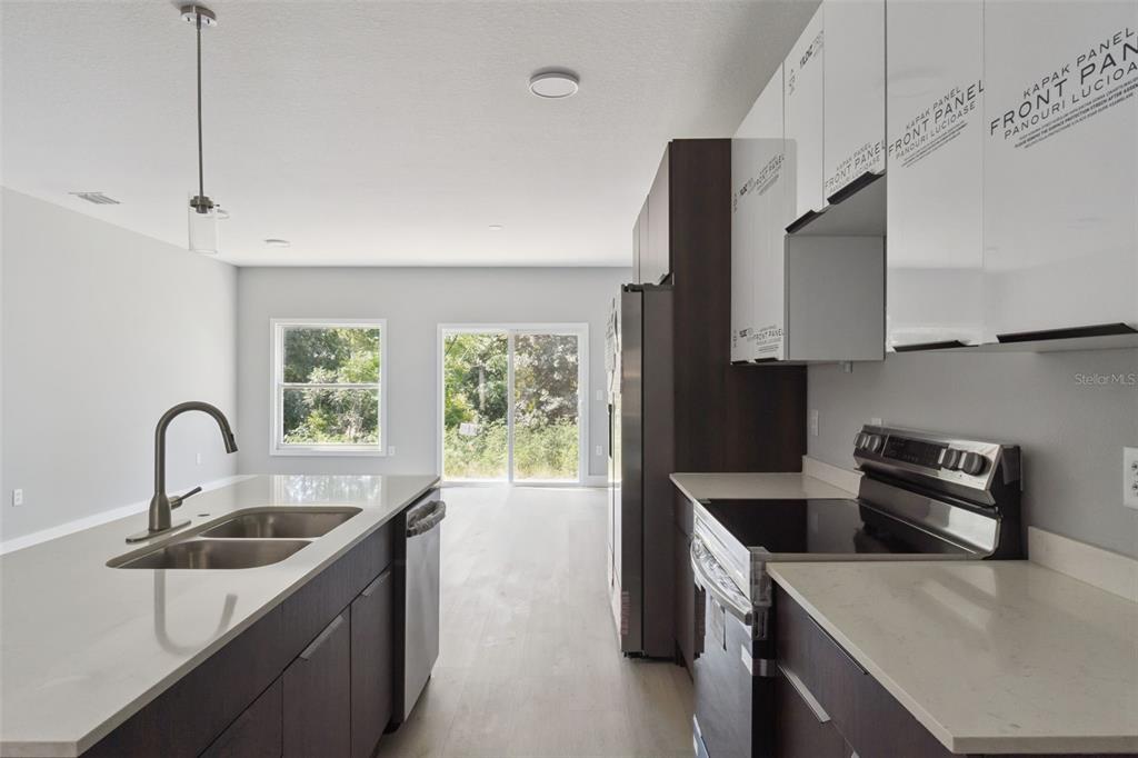 A modern kitchen features dark wood cabinetry, white countertops, stainless steel appliances, and sliding glass doors — 397 NORTH BOULEVARD W, DAVENPORT, FL