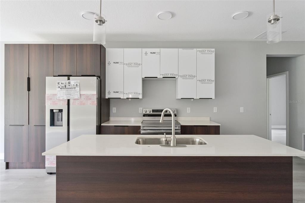 A modern kitchen features dark wood cabinetry, white upper cabinets, a central island, and stainless appliances — 397 NORTH BOULEVARD W, DAVENPORT, FL