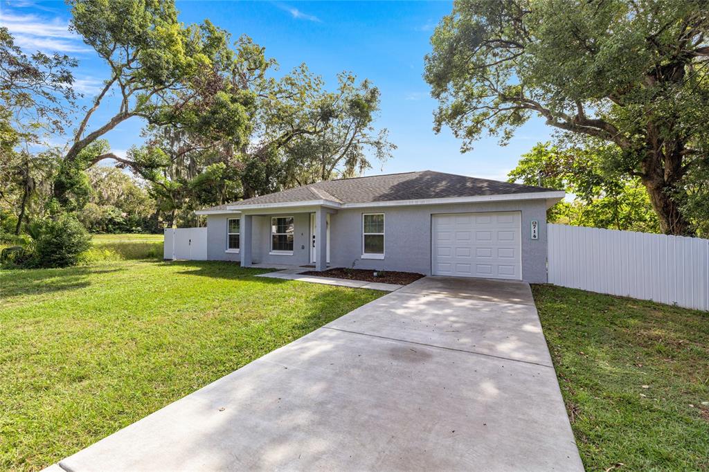 A gray single-story house features a concrete driveway, a one-car garage, and surrounding mature trees — 714 NW 1ST STREET, OCALA, FL