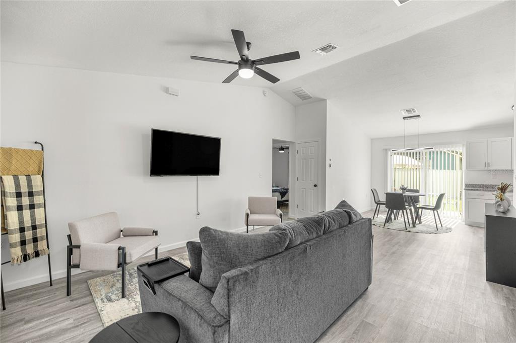 An open-concept living and dining area features light wood-look flooring, white walls, and a ceiling fan — 714 NW 1ST STREET, OCALA, FL