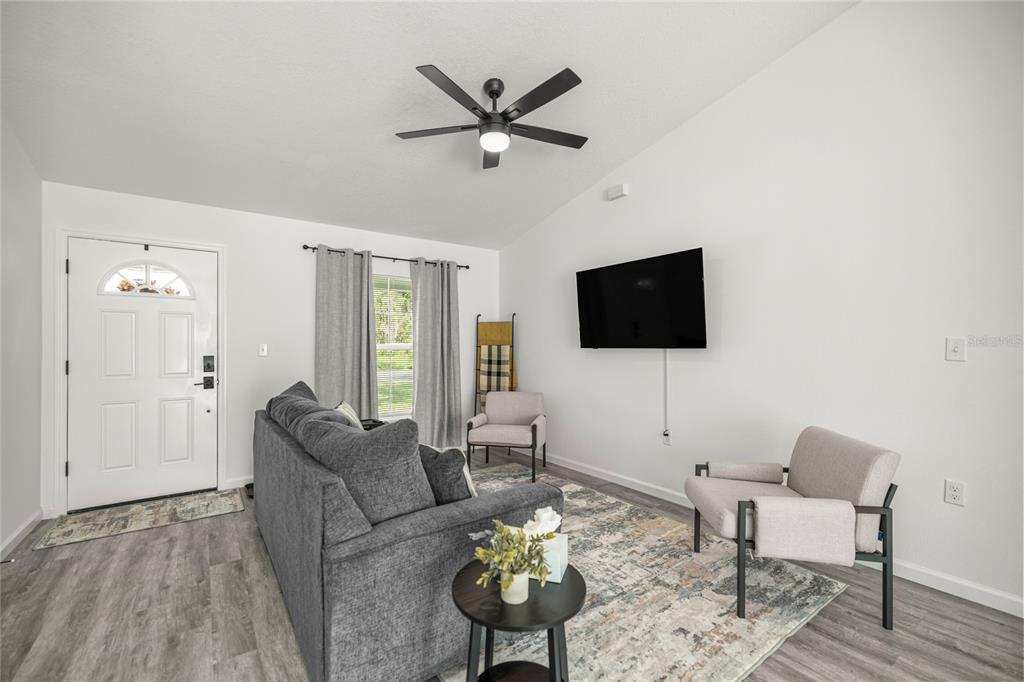 A living room features a gray sofa, two armchairs, a wall-mounted television, and wood-look flooring — 714 NW 1ST STREET, OCALA, FL