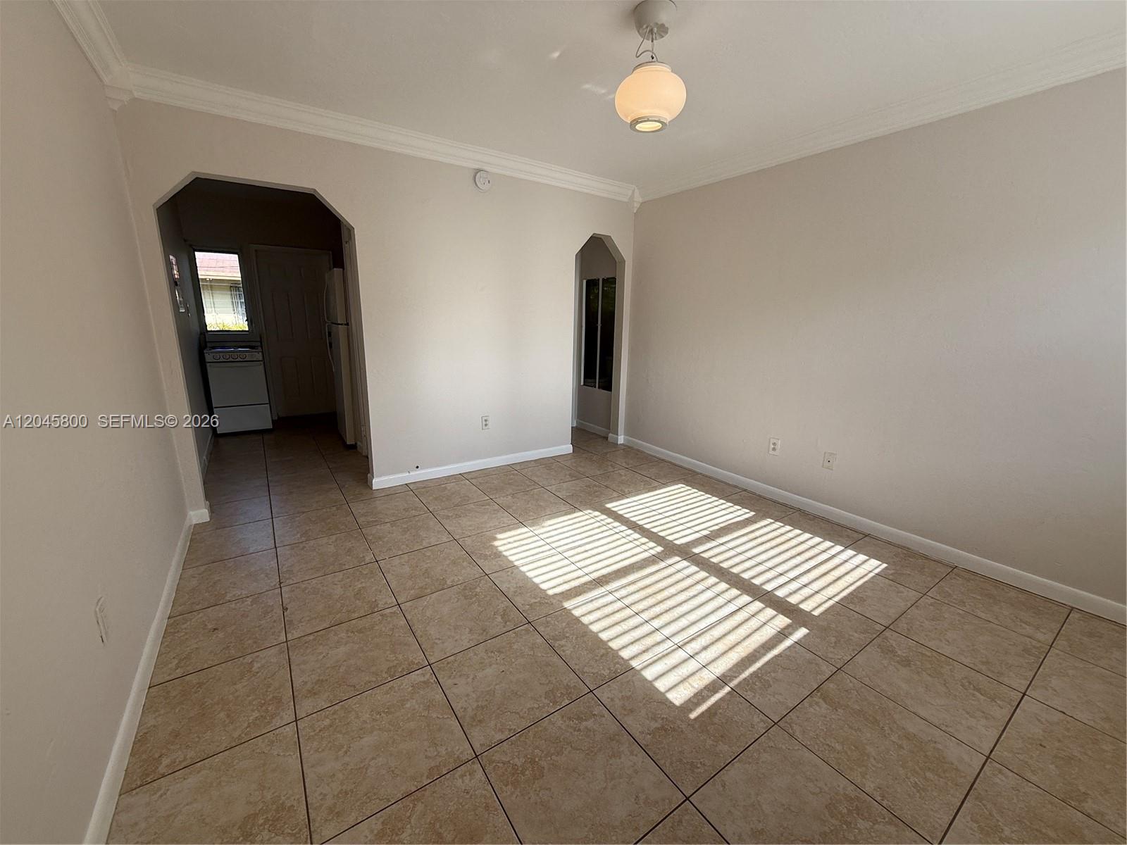 An empty room features beige tile flooring, light-colored walls, and two arched doorways — MIAMI, FL