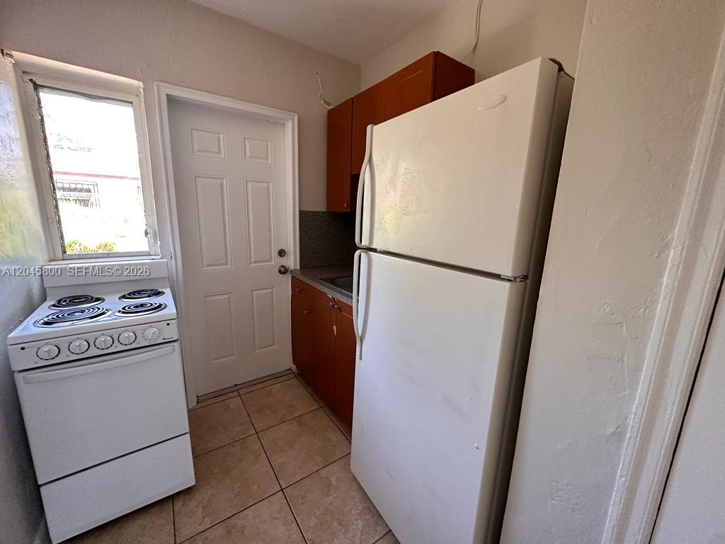 A small kitchen features a white stove, a white refrigerator, and wood-toned cabinets — MIAMI, FL