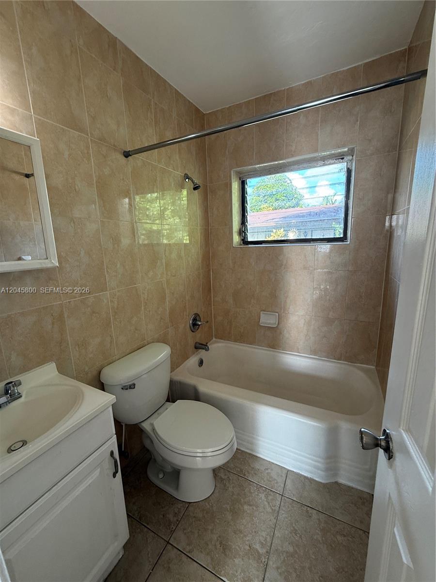 A bathroom features a white vanity, a toilet, and a bathtub with beige tiled walls — MIAMI, FL