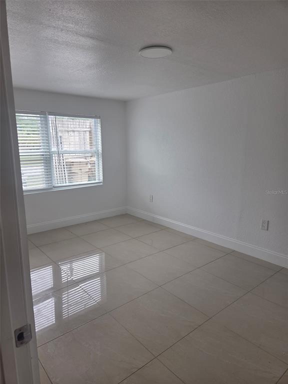 An empty room with white walls, a window with blinds, and light-colored tile flooring — 5930 ALLIGATOR LAKE SHORE W UNIT A2, ST CLOUD, FL