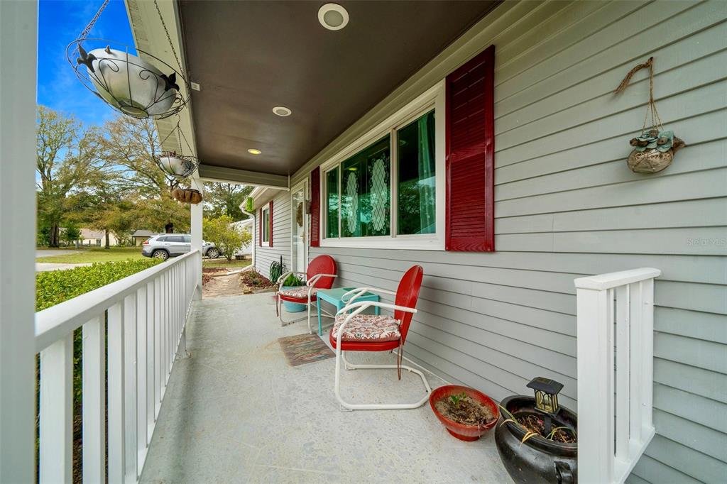 A covered front porch features gray siding, red chairs, and hanging planters — 10821 SW 87TH TERRACE, OCALA, FL