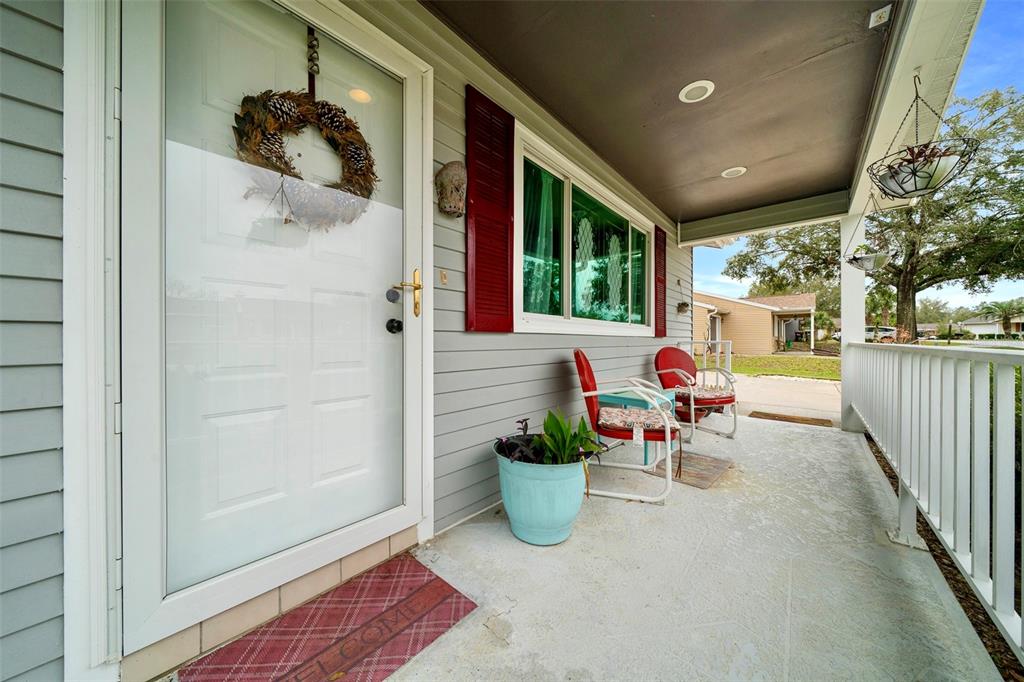 A covered front porch features gray siding, red shutters, a white door, and two chairs — 10821 SW 87TH TERRACE, OCALA, FL