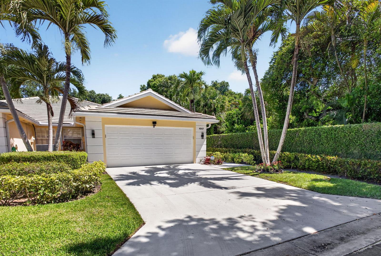 A single-story house with a white garage door, a concrete driveway, and tall palm trees — 4047 Grove Point Road, Palm Beach Gardens FL 33410, PALM BEACH GARDENS, FL