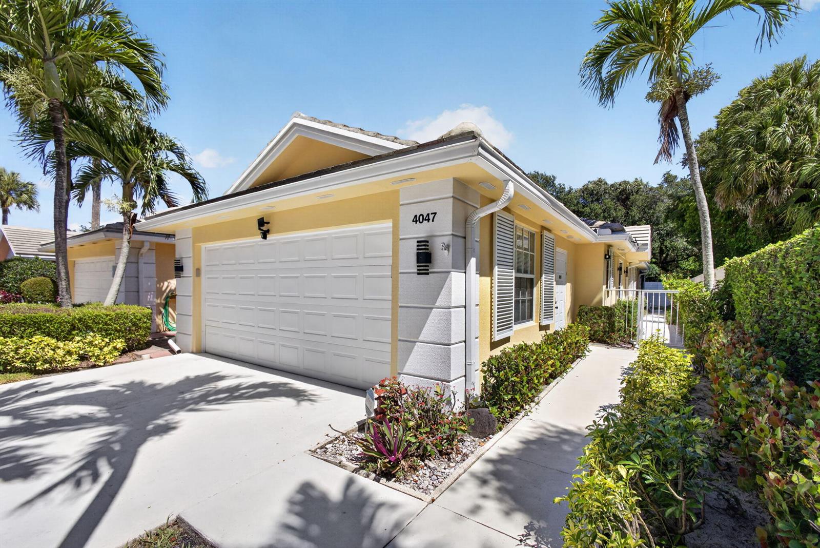 A yellow one-story house features a white garage door, a walkway, and palm trees — 4047 Grove Point Road, Palm Beach Gardens FL 33410, PALM BEACH GARDENS, FL