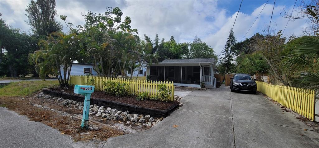 A single-story house with a screened porch, a concrete driveway, and a yellow picket fence — 2912 HAWTHORNE STREET, SARASOTA, FL