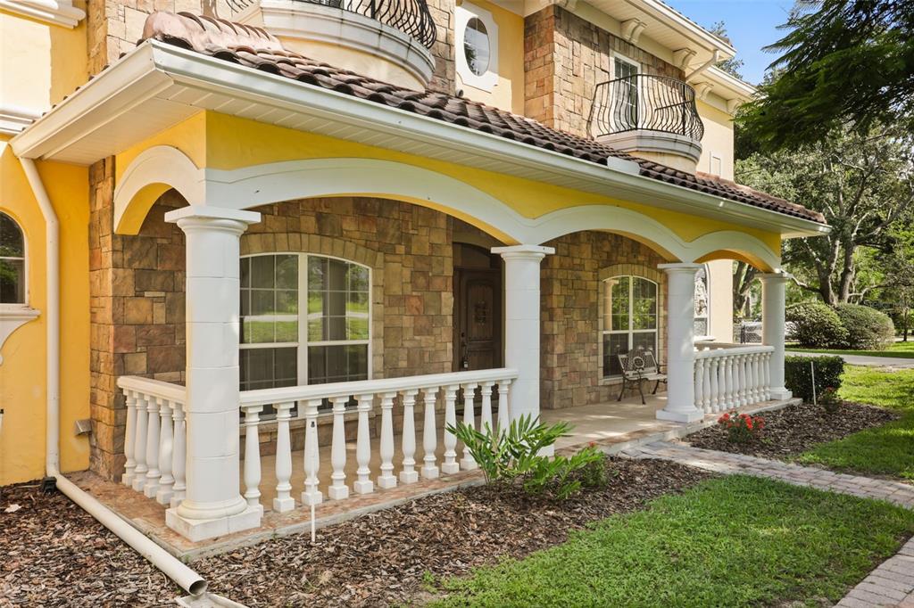 A stone-faced house exterior features a covered front porch with white columns and railings — 5554 PALM LAKE CIRCLE, ORLANDO, FL