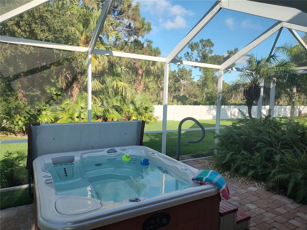 A hot tub sits on a brick patio inside a screened-in lanai overlooking a backyard — 872 CLEAR LAKE DRIVE, ENGLEWOOD, FL