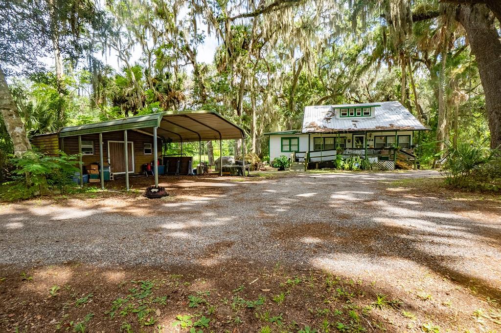A gravel driveway leads to a white cottage with a metal roof and attached carport — 104 W LOUIS BROER ROAD, EAST PALATKA, FL