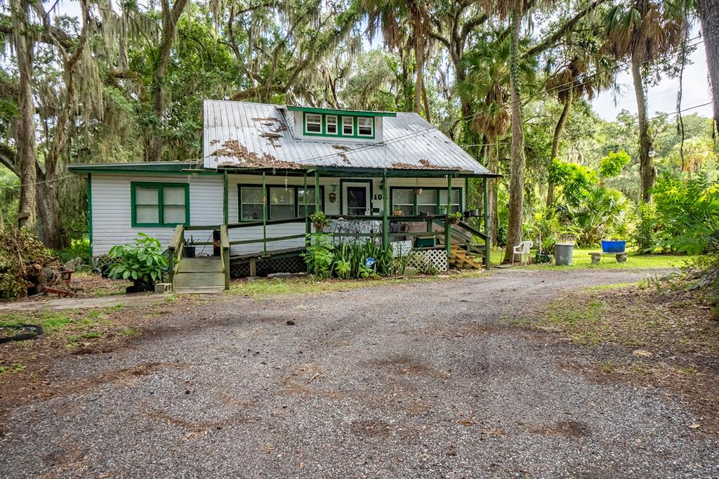 A white cottage with a metal roof and a wooden porch sits on a gravel lot — 104 W LOUIS BROER ROAD, EAST PALATKA, FL