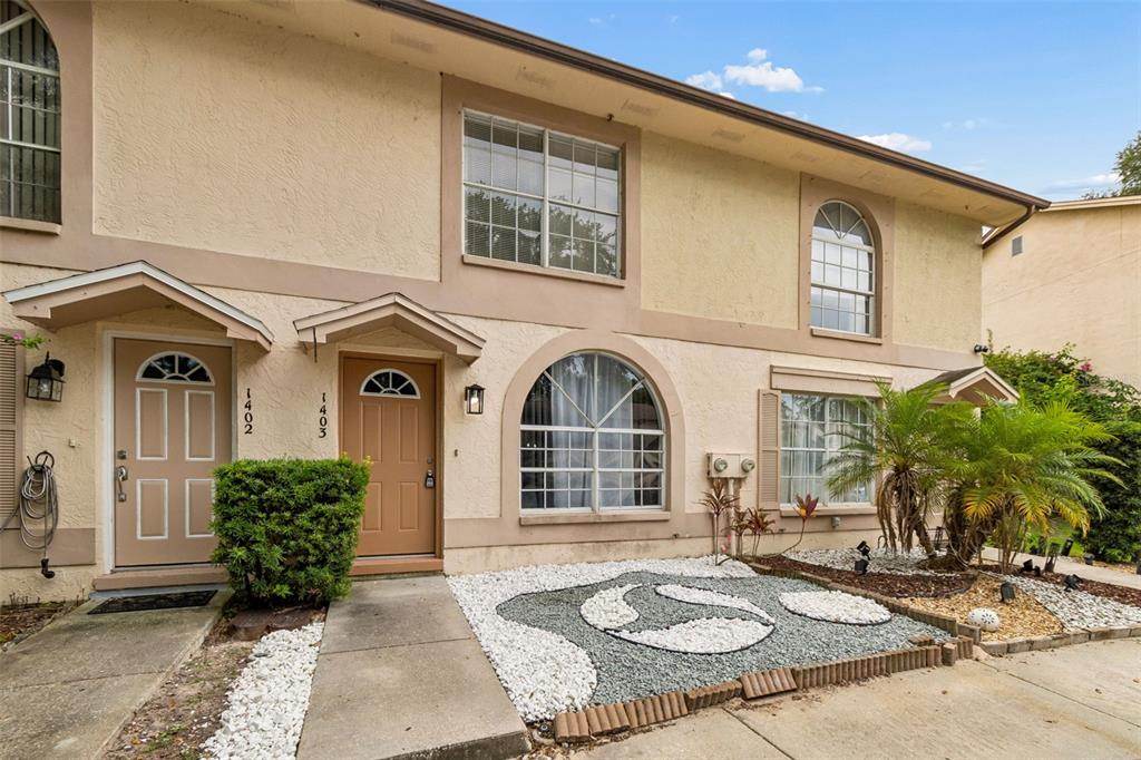 The exterior of a two-story townhouse features tan stucco walls and two adjacent front doors — 1403 BRIGADOON DRIVE, CLEARWATER, FL