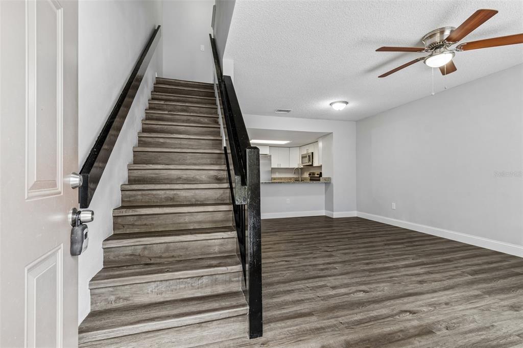 A staircase with wood-look flooring leads upward next to an open living area and kitchen — 1403 BRIGADOON DRIVE, CLEARWATER, FL