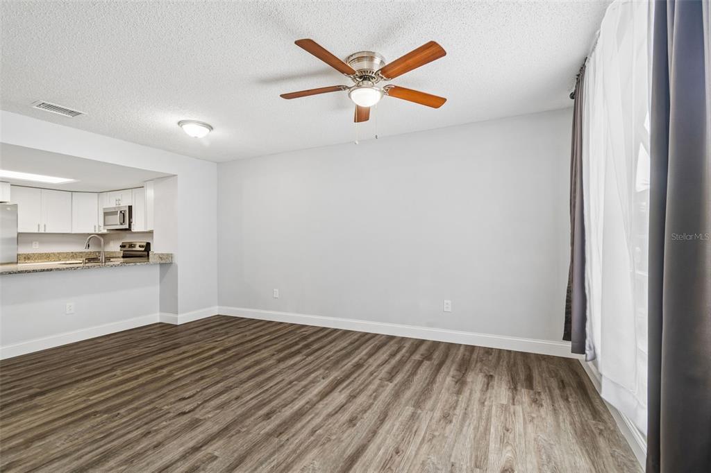 A living room with wood-look flooring, a ceiling fan, and an open view to the kitchen — 1403 BRIGADOON DRIVE, CLEARWATER, FL