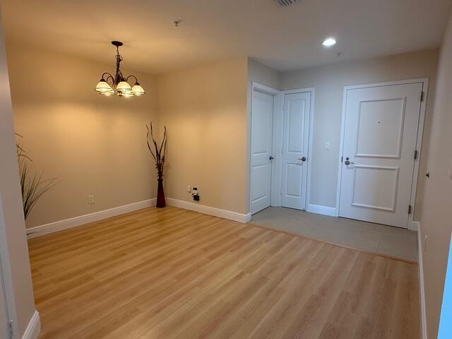 An empty room with light wood flooring, a chandelier, and a white entry door — 1945 S Ocean Drive # 509, Hallandale Beach FL 33009, HALLANDALE BEACH, FL