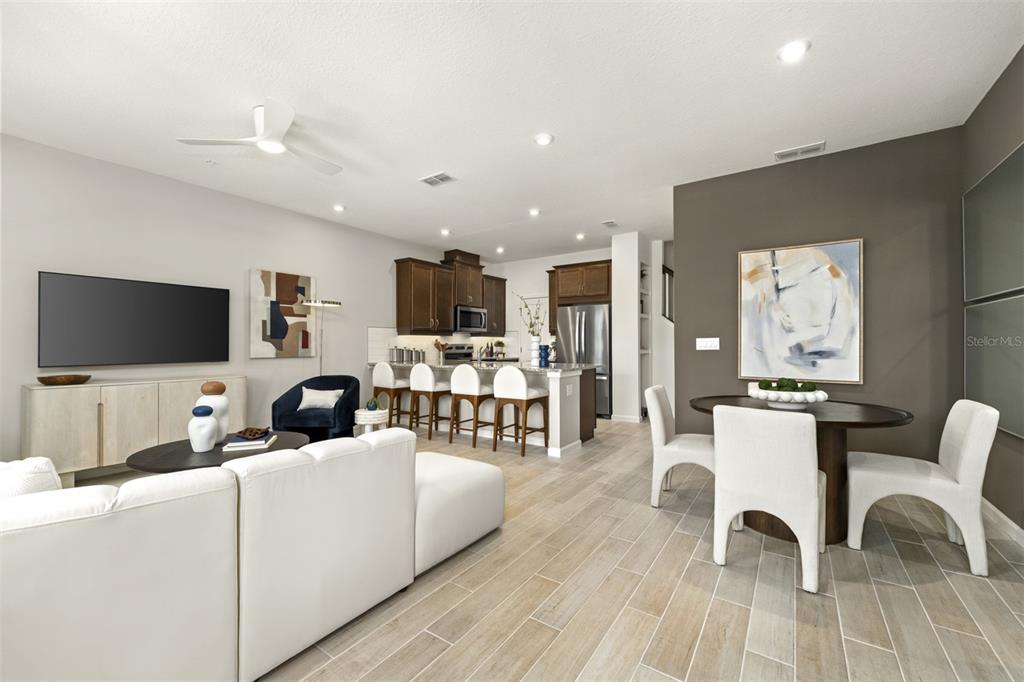 An open-concept living and dining area features white furniture, wood-look tile flooring, and dark cabinetry — 9868 WALKWAY DRIVE, ORLANDO, FL