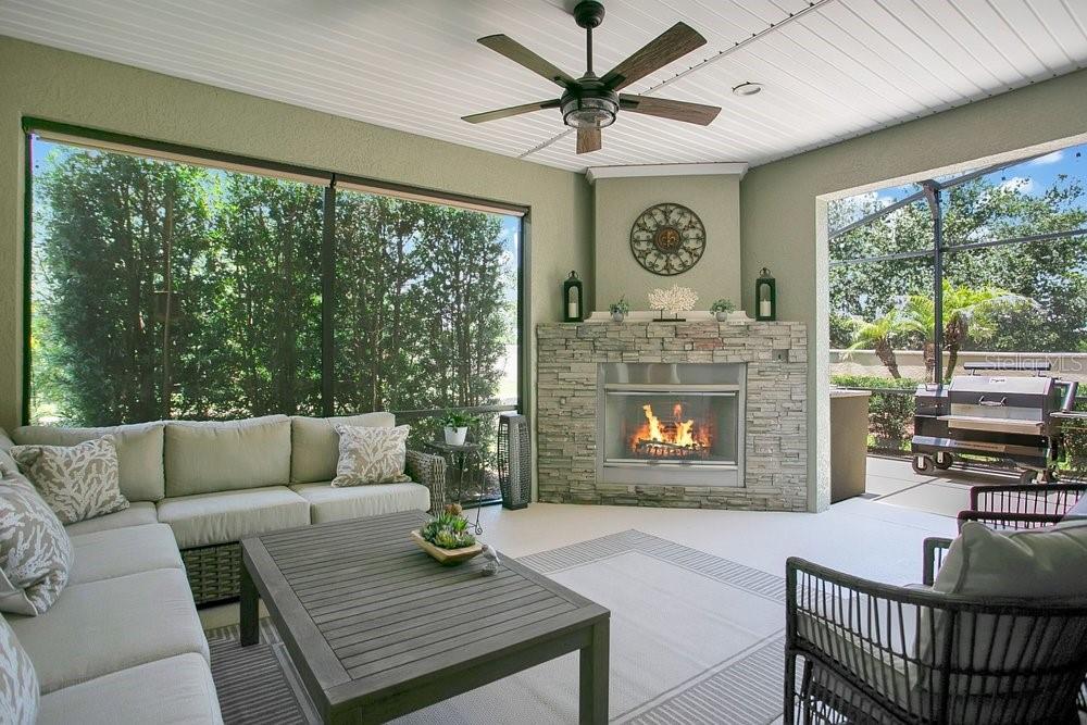 A covered patio features a stone fireplace, outdoor seating, a ceiling fan, and screened walls — 397 SILVER MAPLE ROAD, GROVELAND, FL