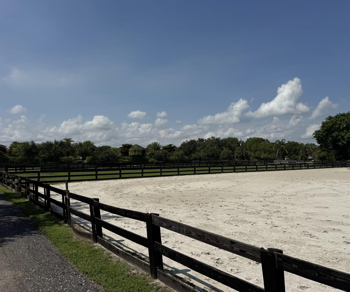 A large, sandy horse riding arena is enclosed by a black wooden post-and-rail fence — 14501 Rolling Rock Place, Wellington FL 33414, WELLINGTON, FL