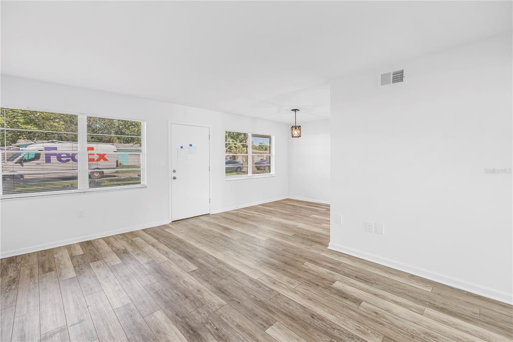 An empty living room features light wood-look flooring, white walls, and a white front door — 1051 79TH AVENUE N UNIT 105, ST PETERSBURG, FL