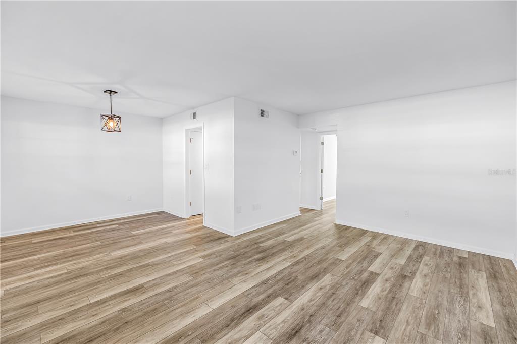 An empty room with white walls, wood-look flooring, and a hanging light fixture — 1051 79TH AVENUE N UNIT 105, ST PETERSBURG, FL