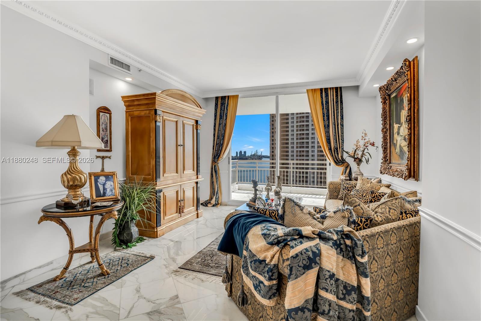 A living room features marble floors, a large wooden armoire, patterned furniture, and a balcony view — 888 Brickell Key Dr # 1807, Miami FL 33131, MIAMI, FL