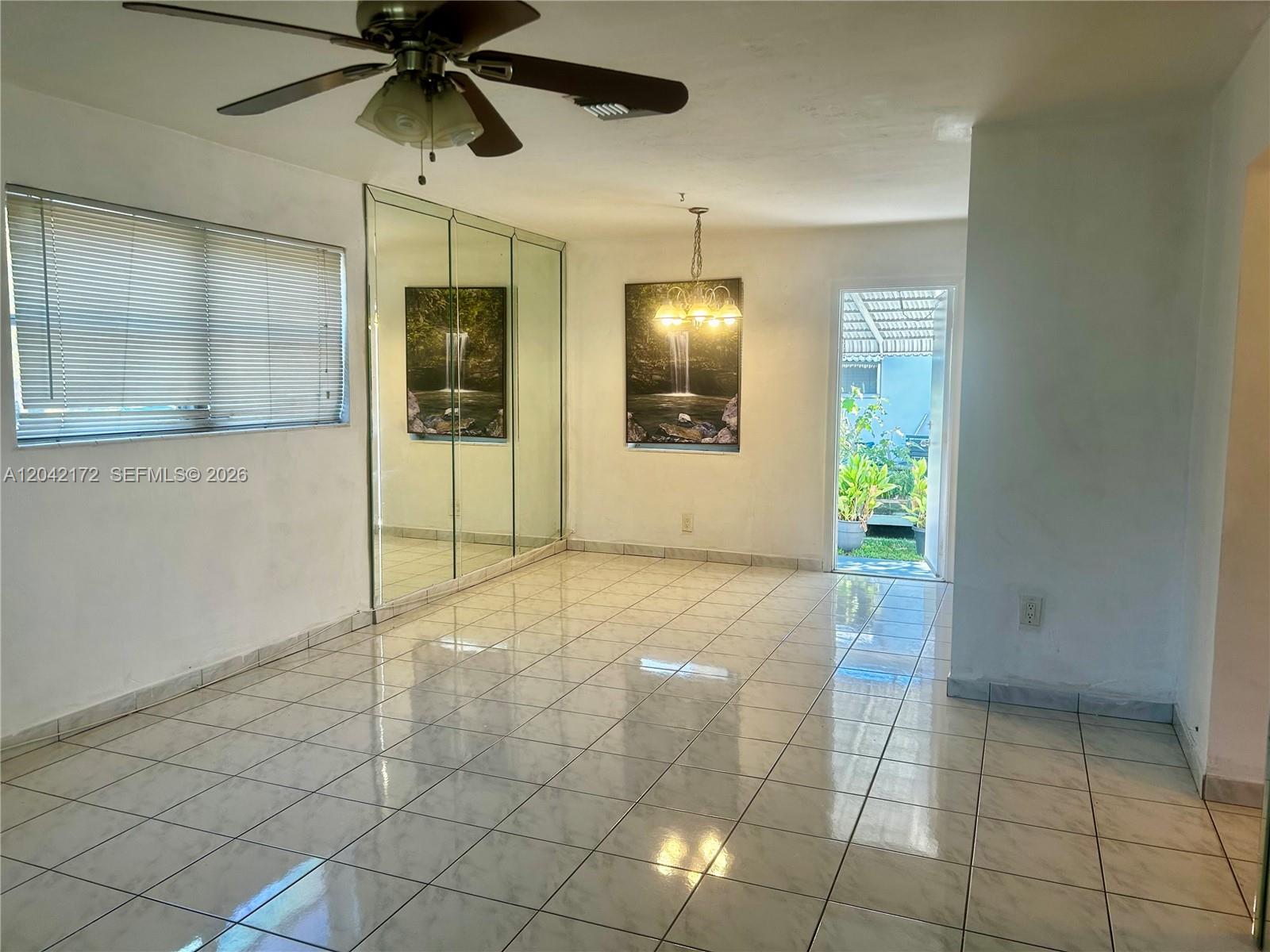 A tiled room features a ceiling fan, mirrored wall panels, and a doorway to outdoors — 2230 Jackson St # 1W, Hollywood FL 33020, HOLLYWOOD, FL