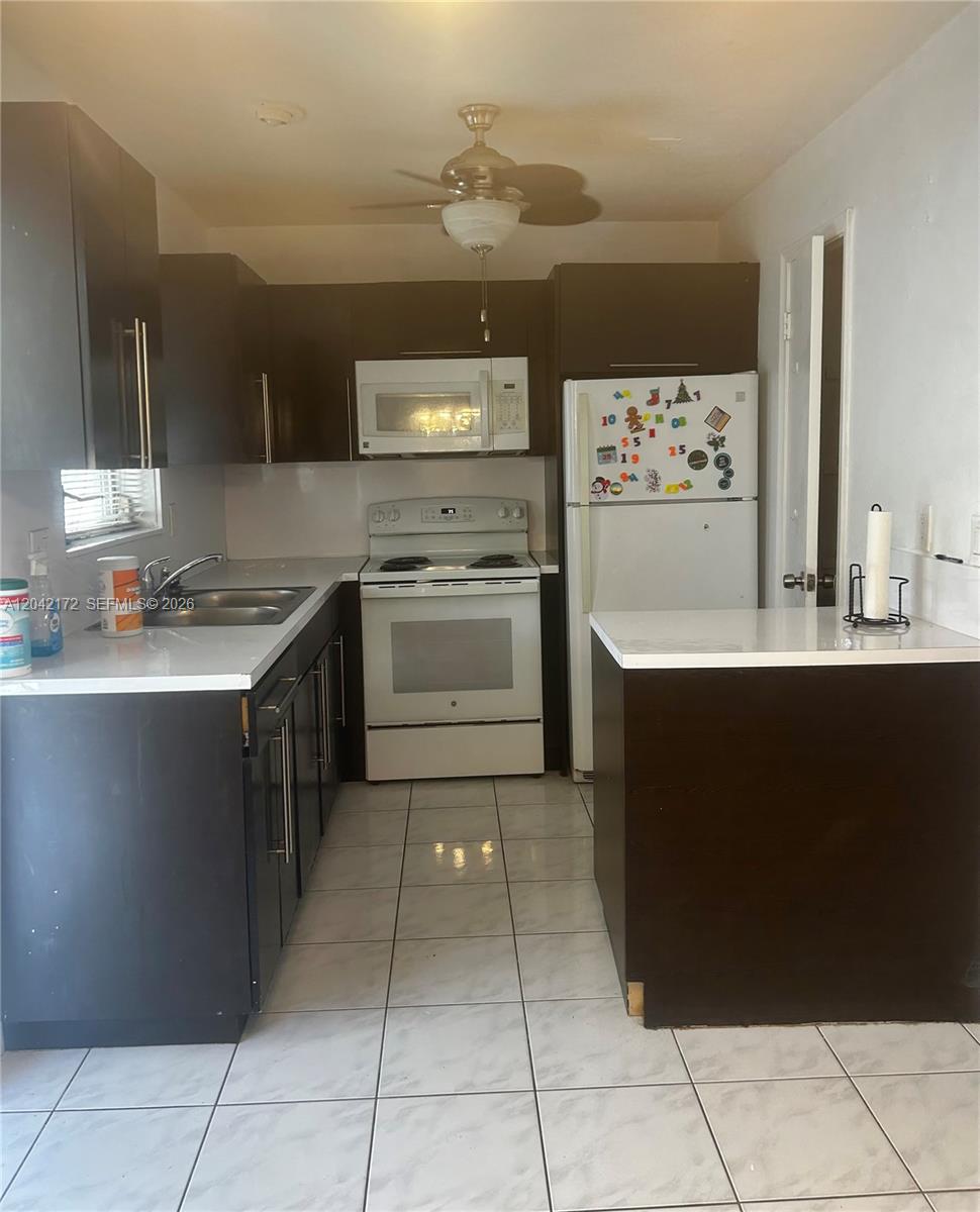 A kitchen features dark brown cabinets, white countertops, white appliances, and light-colored tile flooring — 2230 Jackson St # 1W, Hollywood FL 33020, HOLLYWOOD, FL