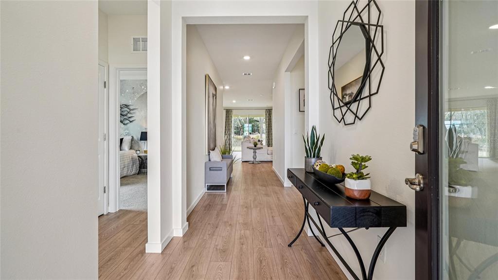 A bright entryway features wood-look flooring, a black console table, and a geometric wall mirror — 3018 CANOPY OAK BOULEVARD, WILDWOOD, FL